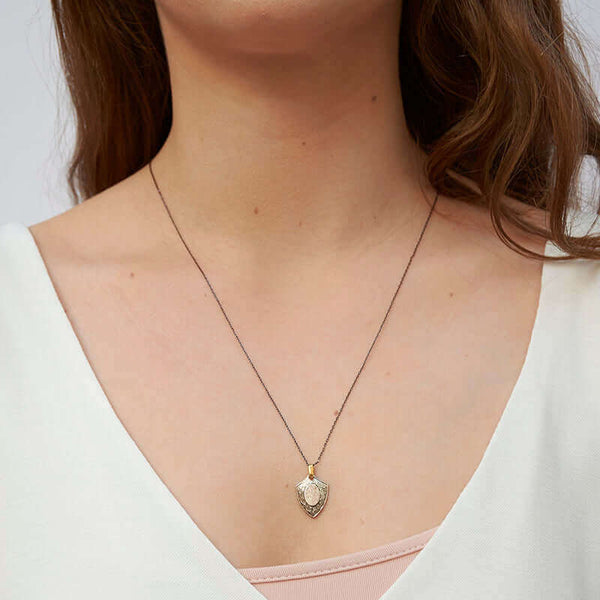 Woman wearing delicate black chain with vintage shield pendant.