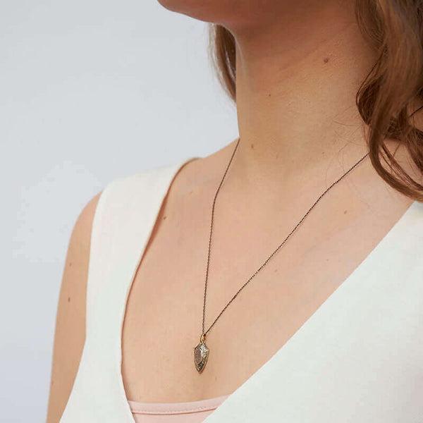 Woman wearing delicate black chain with vintage shield pendant, shown from side angle.