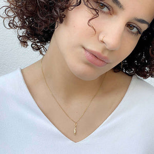 Woman wearing gold necklace with small elongated diamond shaped gold pendant with inset diamond.