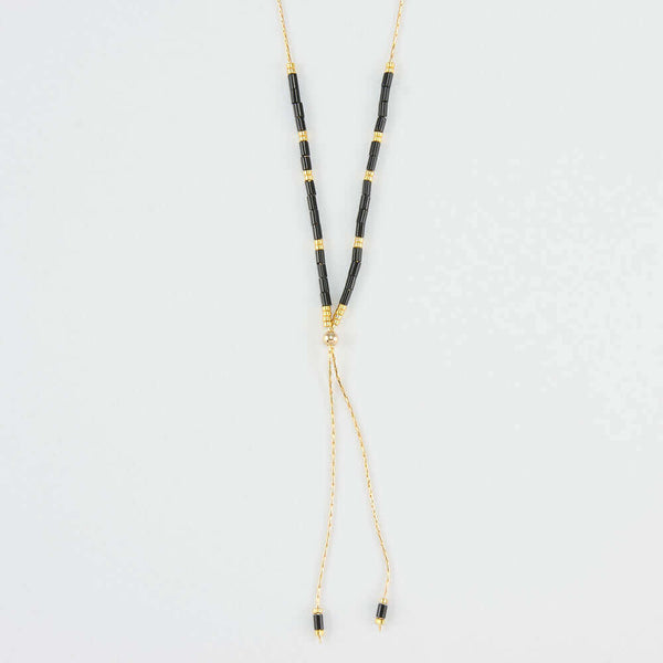 Close-up of delicate gold necklace with black and gold beads shown reverse with adjuster bead.