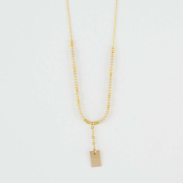 Close-up of delicate gold necklace with white and gold beads and gold rectangle drop pendant.