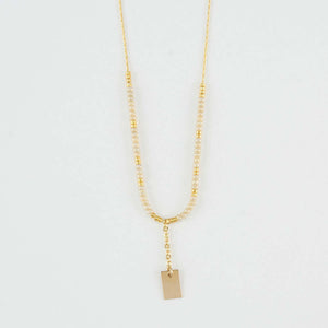Close-up of delicate gold necklace with white and gold beads and gold rectangle drop pendant.