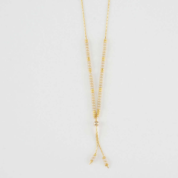 Close-up of delicate gold necklace with white and gold beads shown reverse with adjuster bead.