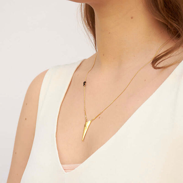 Woman wearing gold chain necklace with chevron pendant, shown from side angle.