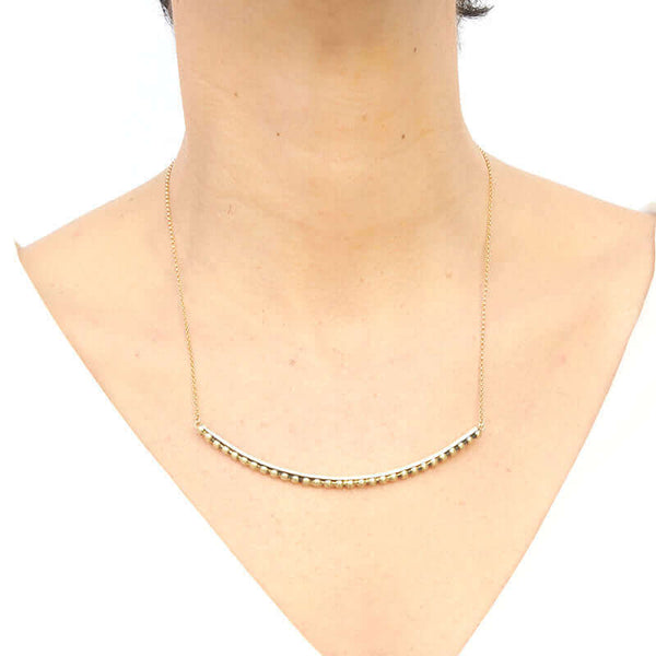 Woman wearing gold chain necklace with beaded curved bar at bottom, worn long.