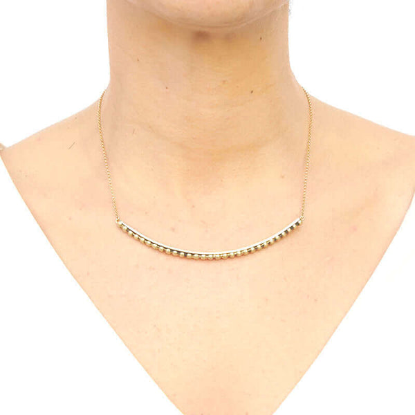Woman wearing gold chain necklace with beaded curved bar at bottom, worn short.