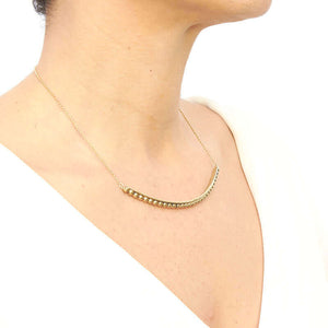 Woman wearing gold chain necklace with beaded curved bar at bottom, shown from side angle.