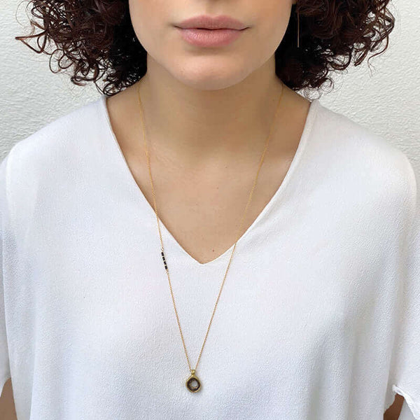 Woman wearing delicate gold chain necklace with carved round pendant.