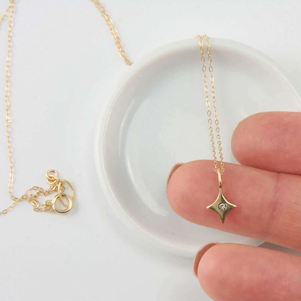 Close-up of fingers holding 4 point gold star pendant  with inset diamond on delicate gold chain necklace.