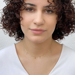 Woman wearing delicate gold chain necklace with 5 small vertical bar accents on bottom.