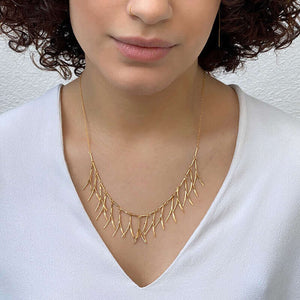 Woman wearing delicate gold necklace with curved hanging frill design.