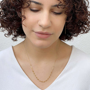 Woman wearing delicate gold chain necklace with bead chain detail at bottom.