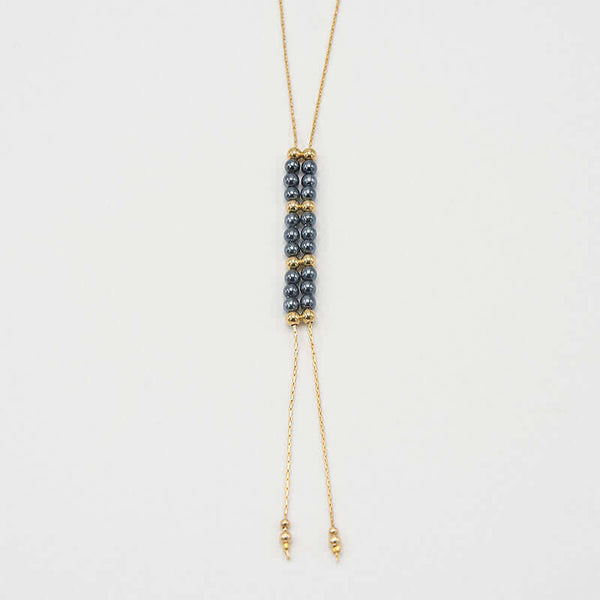 Close-up of gold chain necklace with pendant of double rows of dark pearls and gold beads, that slide to adjust length.