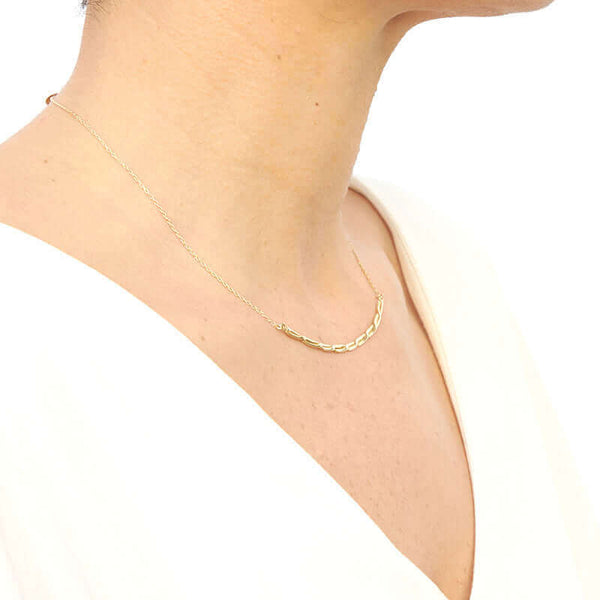 Woman wearing gold chain necklace with cast twisted rope bar pendant, shown from side angle.