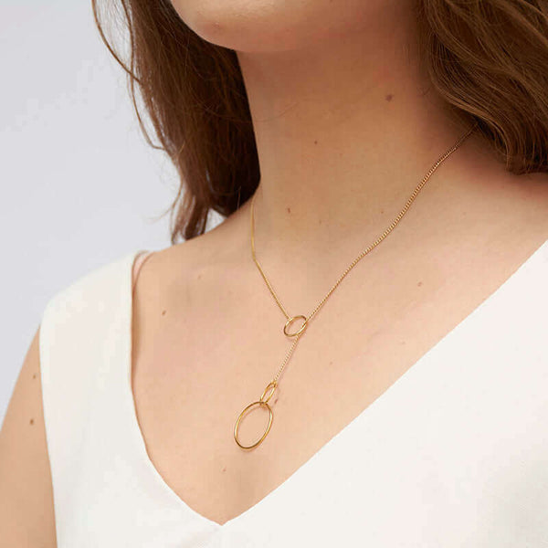 Woman wearing gold chain necklace with hoops are at end that slide for adjustment, shown at side angle
