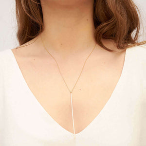 Woman wearing gold chain necklace with long flattened wire pendant.