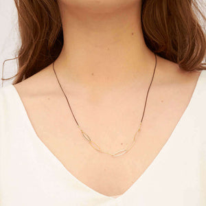 Woman wearing black oxidized silver necklace with oval gold links on the bottom.