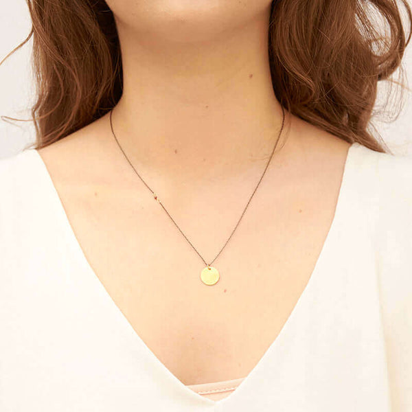 Woman wearing black oxidized silver necklace with round brushed gold pendant.
