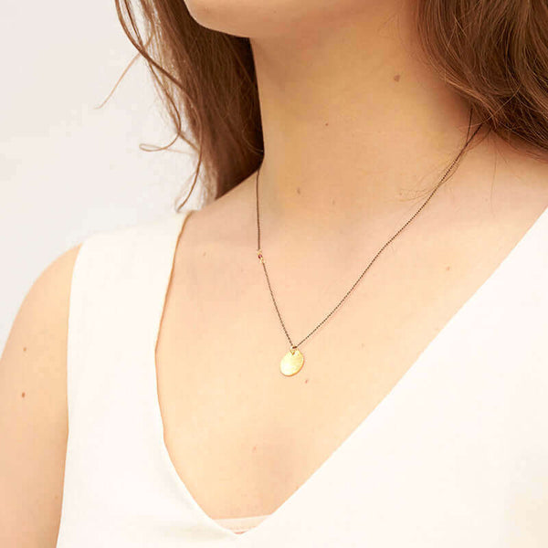 Woman wearing black oxidized silver necklace with round brushed gold pendant, shown side angle.