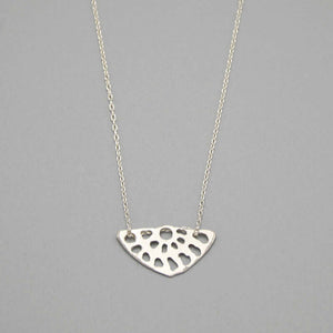 Close-up of delicate silver chain necklace with lotus root motif pendant.