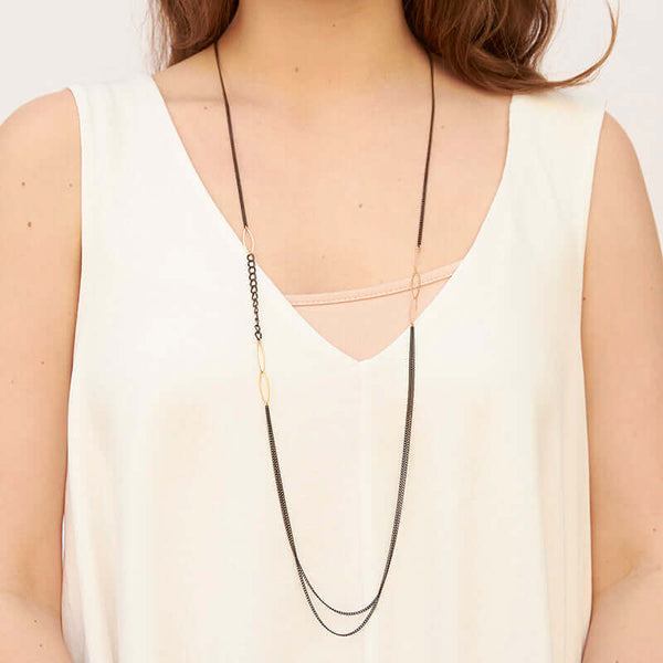Woman wearing long black oxidized silver multi-chain necklace with gold link details along chain.