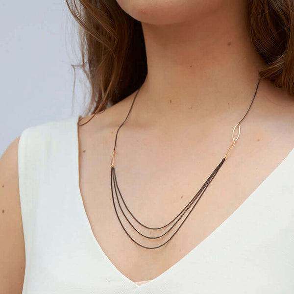 Woman wearing short black oxidized silver multi-chain necklace with gold link details along chain, shown side angle.