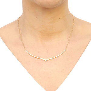 Woman wearing gold necklace with curved bar pendant with geometric native motif.