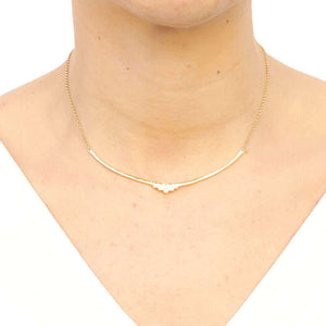Woman wearing gold necklace with curved bar pendant with geometric native motif.