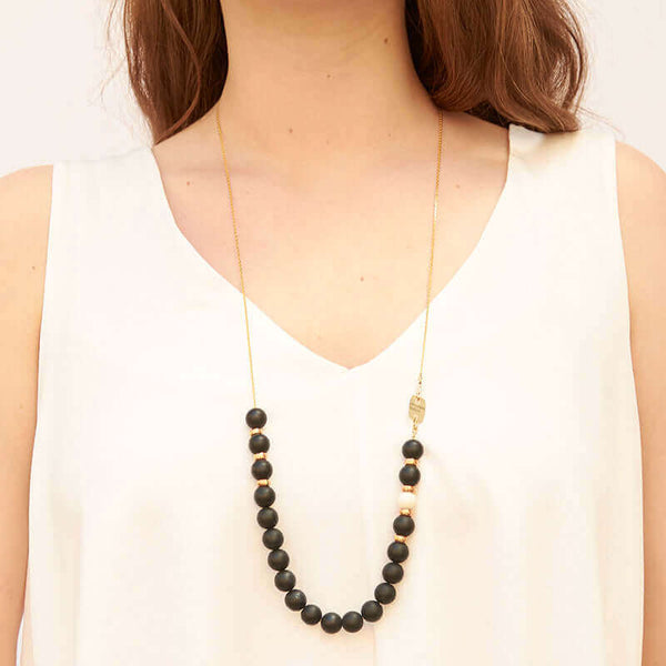 Woman wearing gold chain with frosted onyx beads with single white bead and brass bead details.