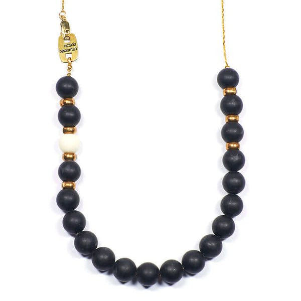 Close-up of gold chain with frosted onyx beads with single white bead and brass bead details.