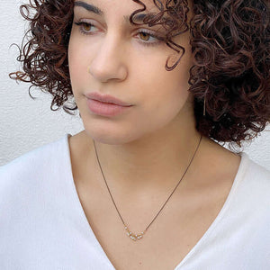 Woman wearing delicate black oxidized necklace with small pearls as pendant.