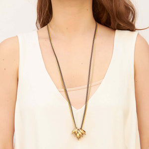 Woman wearing gold and dark multi-chain necklace with 5 heavy brass links as pendant.