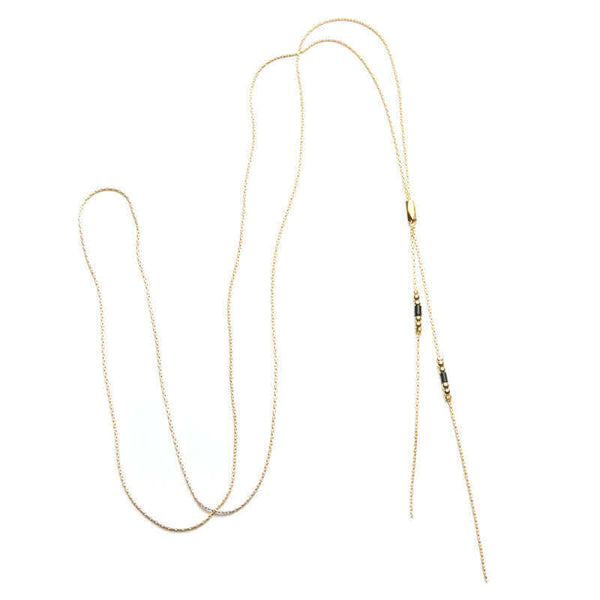 Delicate gold chain lariat style bracelet with slider bead and black bead details near ends.