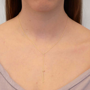 Woman wearing dainty gold necklace with pendant of simple drop chain and bar.