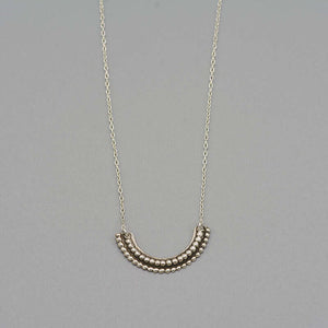 Close-up of silver necklace with beaded curved pendant.