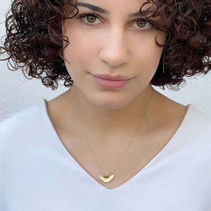 Woman wearing dainty gold necklace with fan shaped pendant.