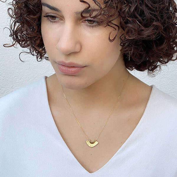Woman wearing dainty gold necklace with fan shaped pendant.