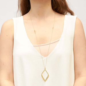 Woman wearing long gold necklace with rhombus shaped pendant.