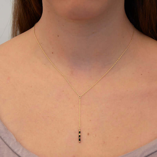 Woman wearing dainty gold necklace with pendant of simple drop chain and black beads.
