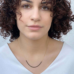 Woman wearing gold necklace with black tubes and gold beads on bottom hanging short.