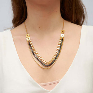 Woman wearing multi-chain necklace with dark and gold chains hanging from small box chain with square links on side.
