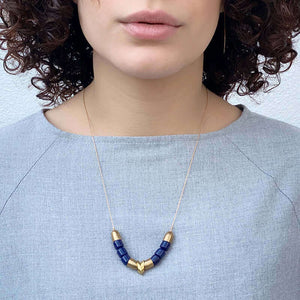 Woman wearing gold necklace with brass cups, links, and blue beads as pendant.