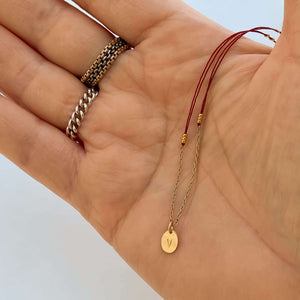 Close-up of hand with delicate red thread necklace with gold chain and oval pendant.