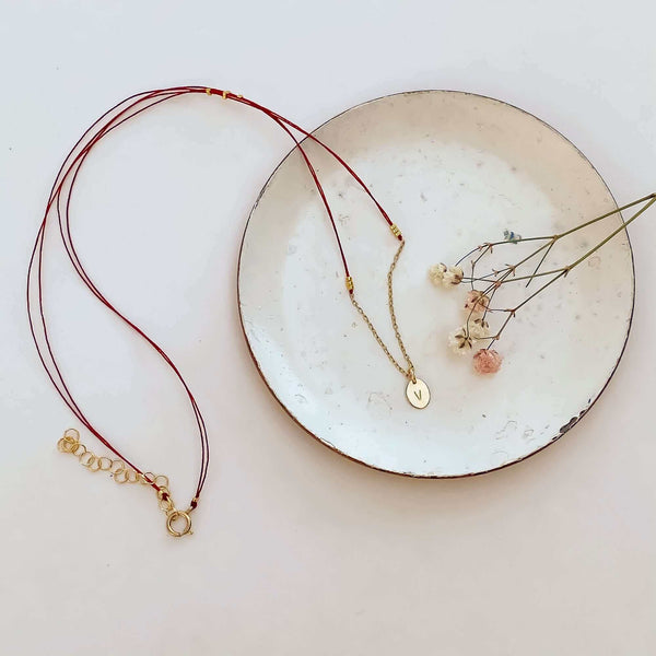 Delicate red thread necklace with gold chain and oval pendant on small plate.