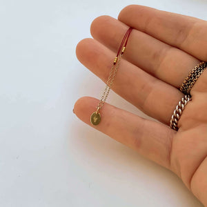 Close-up of fingers with delicate red thread necklace with gold chain and oval pendant.