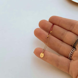 Close-up of hand with delicate red thread necklace with gold chain and oval pendant.