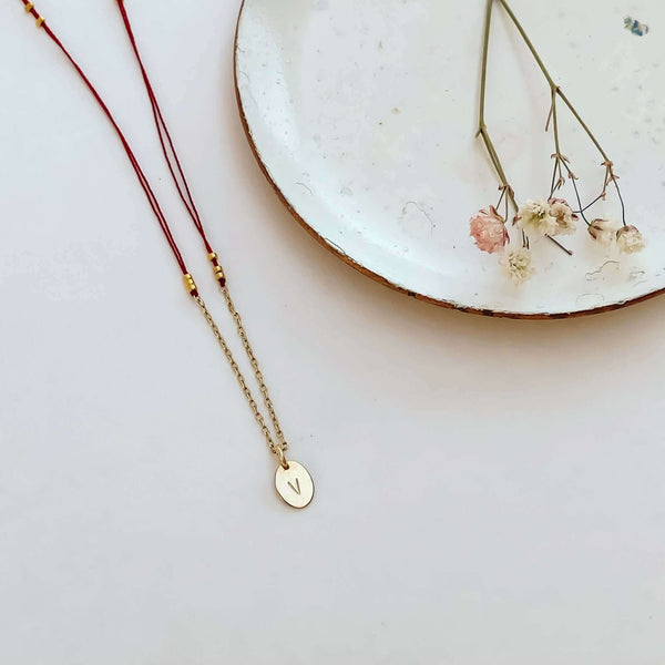 Close-up of delicate red thread necklace with gold chain and oval pendant with plate with small flowers.
