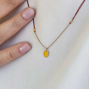 Woman wearing necklace red thread necklace with gold chain and oval pendant.