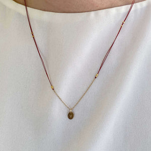 Woman wearing necklace red thread necklace with gold chain and oval pendant.