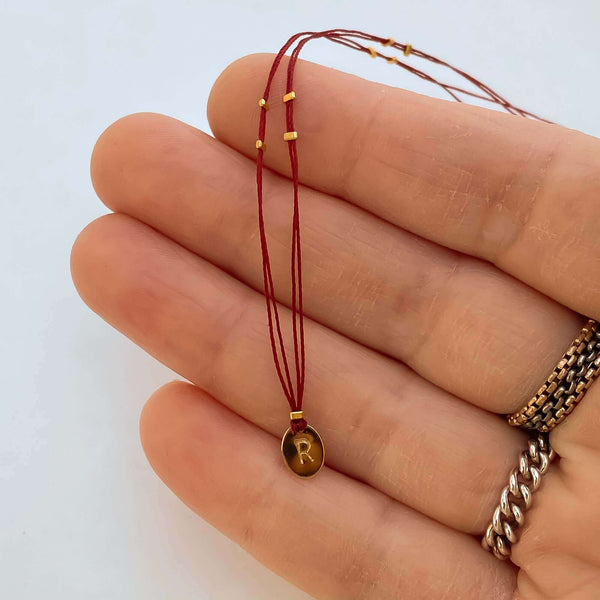 Close-up of fingers with delicate red thread necklace with gold accents and oval pendant.